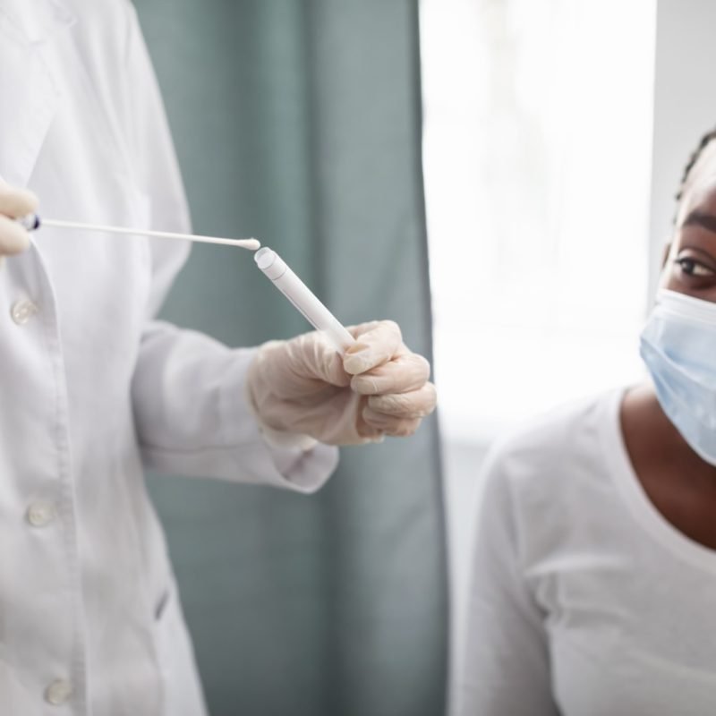 PCR Testing For Covid-19. Doctor holding and inserting cotton swab in tube after taking coronavirus sample from nose and throat of potentially infected black woman. Diagnostic And Analysis